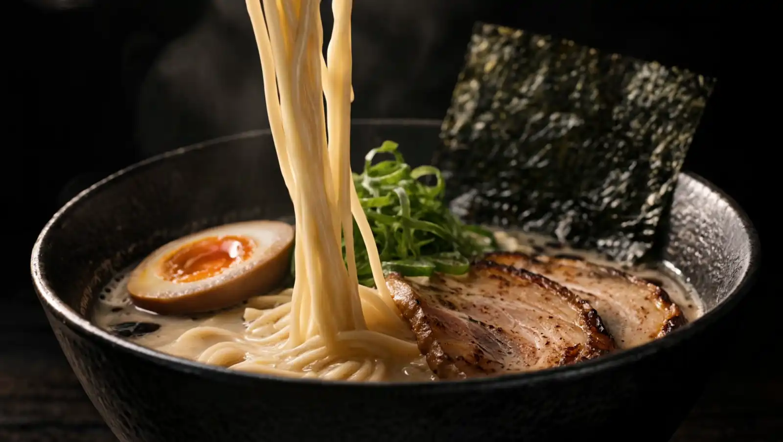 Chopsticks lift a tangle of thin noodles out of the bowl, steam rising.